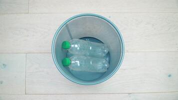 Six plastic bottles of different colors and volumes in turn fall into the office trash can. One transparent bottle does not hit the trash and rolls out of the frame video