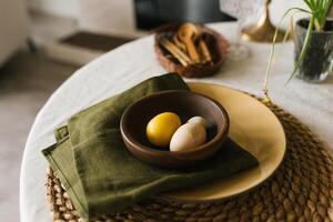 Table with a green napkin and a yellow bowl with easter eggs on it photo