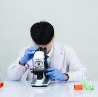 retrato asiático hombre estudiante científico médico vestido uno persona sti en laboratorio mirando mano participación prueba tubo químico. causado por mezcla reactivos en científico investigación laboratorios y microscopio en mesa foto