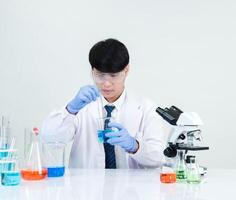 retrato asiático hombre estudiante científico médico vestido uno persona sti en laboratorio mirando mano participación prueba tubo químico. causado por mezcla reactivos en científico investigación laboratorios y microscopio en mesa foto