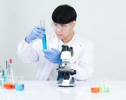 retrato asiático hombre estudiante científico médico vestido uno persona sti en laboratorio mirando mano participación prueba tubo químico. causado por mezcla reactivos en científico investigación laboratorios y microscopio en mesa foto