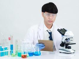 retrato asiático hombre estudiante científico médico vestido uno persona sti en laboratorio mirando mano participación prueba tubo químico. causado por mezcla reactivos en científico investigación laboratorios y microscopio en mesa foto