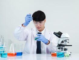 retrato asiático hombre estudiante científico médico vestido uno persona sti en laboratorio mirando mano participación prueba tubo químico. causado por mezcla reactivos en científico investigación laboratorios y microscopio en mesa foto