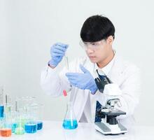 retrato asiático hombre estudiante científico médico vestido uno persona sti en laboratorio mirando mano participación prueba tubo químico. causado por mezcla reactivos en científico investigación laboratorios y microscopio en mesa foto