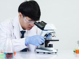 retrato asiático hombre estudiante científico médico vestido uno persona sti en laboratorio mirando mano participación prueba tubo químico. causado por mezcla reactivos en científico investigación laboratorios y microscopio en mesa foto