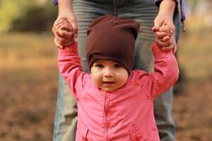 Portrait of a cute baby girl holding mom's hands and learning to walk in the spring park photo