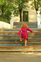 Purposeful toddler girl in pink dress reaching the top of old blue vintage stairs photo