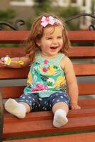 One year old sweet girl sitting on a wooden bench and laughing out load in a lovely summer evening photo