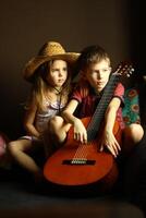 Portrait of sitting caucasian children, wearing western style straw hat and holding the guitar photo