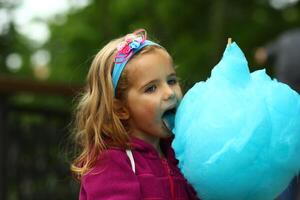 Closeup portrait of happy toddler girl eating bright blue cotton candy photo