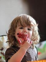 uno año antiguo bebé niña comiendo delicioso arándano y negro grosella tarta con su cara sucio todas encima. foto