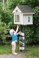 Little girl trying to get a book out of a community public street library. Book crossing. photo