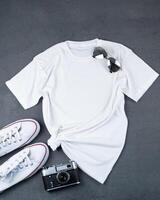 White T-shirt with place for text. Sneakers, glasses, camera - a set of clothes for walking. T-shirt mockup for printing. Stylish kit. Grey background with copy space photo