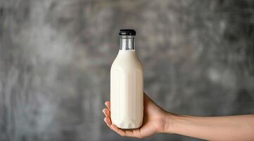 AI generated Hand holding bottle of milk on gray background. With space for add text. photo