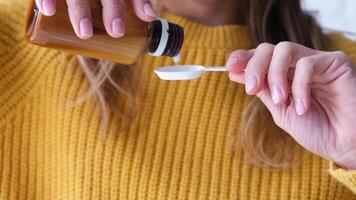 healthcare, treatment and medicine concept. woman in yellow sweater pouring medication or antipyretic syrup from bottle to spoon video