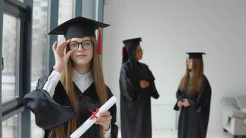 One student in a master's robe stands in front of the camera, and two students communicate in the background. Prosess of university studies. Master of Science video