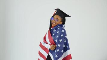 Happy stylish afro american female student in graduate uniform dancing holding usa flag over shoulders. Education of USA video