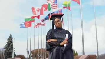 joven africano americano mujer se regocija con un diploma de mayor educación en su mano en pie en contra el cielo y banderas de diferente países revoloteando en el viento. Maestro de leyes video