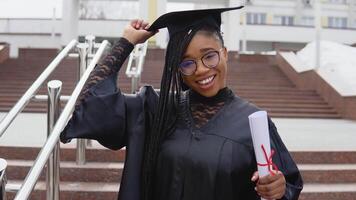 une Jeune femme à le Université à le maîtrise manteau détient une diplôme avec un main et une chapeau avec un autre. Maître de science regards à le caméra. Maître de pharmacie video