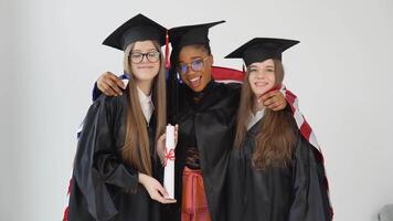 Tres mujer estudiantes de Estados Unidos Universidad son vistiendo graduarse trajes y sombreros. uno de ellos sostiene un diploma de maestría la licenciatura video