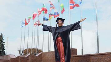 ung afrikansk amerikan kvinna gläds med en diplom av högre utbildning i hand på de gata mot de bakgrund av flaggor av annorlunda länder i Europa och de värld. bemästra av apotek video