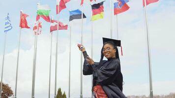 A young African-American woman rejoices and points with a diploma to the flags of different countries fluttering in the wind video