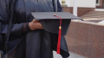 Master's hat with a red tassel on the hand of a university graduate. Close up view with an outdoor stairs onbackground video