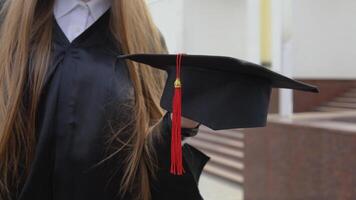 mästare hatt med en röd tofs på de hand av en universitet examen. stänga upp se med en utomhus- bakgrund video