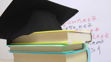 The black square hat of the master lies on the textbooks stacked in a column. The attributes of a university graduate revolve around its axis on a stand video