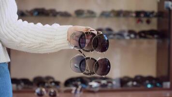 Three pairs of glasses in a female hand on a background of a shelf with glasses video