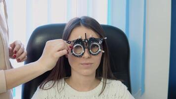 A doctor installs glass in a skiascope for a young Caucasian woman in a cozy white sweater at an optics clinic video