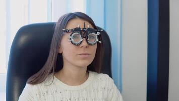 een jong vrouw in een knus wit trui in de oogarts kantoor Bij de optiek kliniek antwoorden een vraag van een oogarts. video