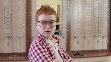 een roodharig jongen in een plaid rood en wit overhemd staat met transparant bril voor visie correctie draaide zich om zijn schouder naar de camera met en vouwen zijn handen in de slot video