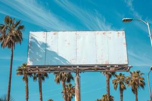 AI generated An empty billboard stands tall under a clear blue sky, flanked by towering palm trees, offering a perfect canvas for advertising photo