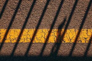 Asphalt sidewalk surface with worn yellow line and striped shadow striped pattern as background photo