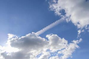 Aircraft condensation contrails in the blue sky inbetween some clouds photo