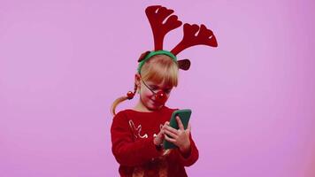 Girl child in Christmas deer antlers looking smartphone display sincerely rejoicing win success luck video
