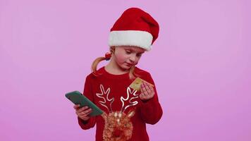 Girl in Christmas sweater using credit bank card smartphone while transferring money shopping online video