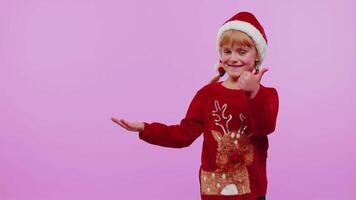 Girl child in Christmas sweater deer showing thumbs up and pointing at on blank advertisement space video