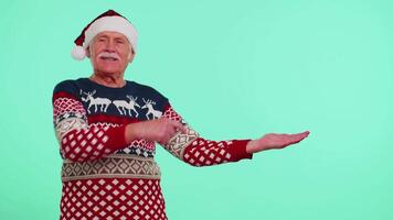 Grandfather in Christmas deer sweater showing thumbs up and pointing at on blank advertisement space video
