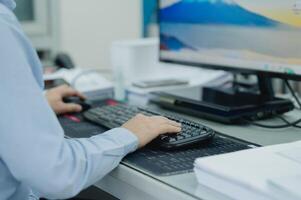 Businessperson or is typing on a computer keyboard. The person is wearing a blue shirt and is using a black keyboard in office photo