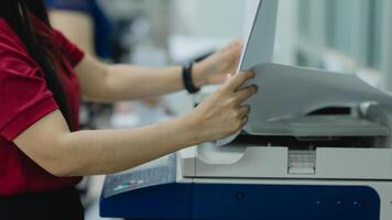 A woman is using a printer to print a document. She is wearing a red shirt and is holding a piece of paper in her hand photo