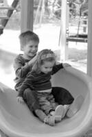 Kids having fun because of hair raising static electricity on the plastic playground slide. Black and white portrait photo