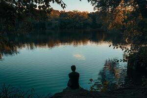 AI generated A person sits peacefully at the edge of a calm body of water, lost in thought and introspection. photo