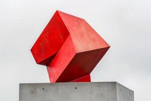 ai generado un vibrante rojo geométrico escultura esmeradamente descansa en un cemento bloquear. foto