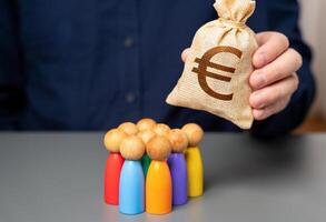A businessman holds a euro money bag near a group of people figurines. Preferential loans for entrepreneurs and businesses. Allocation of budget money for projects. Social support. photo