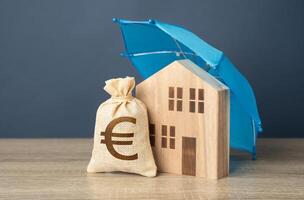 House with euro money bag and blue umbrella. Property insurance. Financial security. Protect investment and be prepared for unforeseen events. Repairs or rebuilding in the event of a covered loss. photo