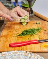 Chef's hands cutting fresh zucchini on a wooden board in the kitchen photo