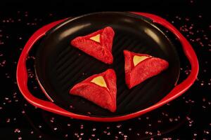 Hamans ears - hamantash are red, with Red Velvet flavor, on a black-red plate against a background with reflection photo