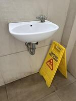 Caution wet floor yellow warning board under the sink with blue floor dryer in public toilet photo